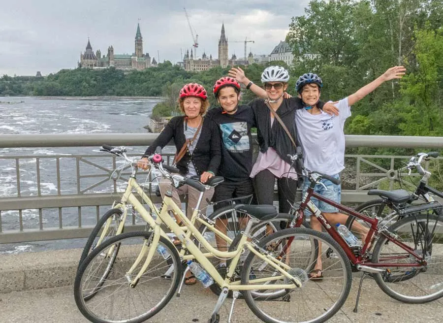 Family is biking on Ottawa river pathway with parliament building view during their Express tour by bike in Ottawa