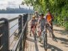 Parents and kids cycling on a wooden bridge with the view of Ottawa river and parliament building on an Ottawa express tour